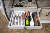 RV rental kitchen: A drawer brimming with organized utensils, cooking tools. Above, a compact stove; to the side, a cooler.