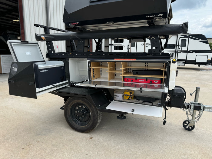 Compact RV rental trailer featuring an open outdoor kitchen with Dometic fridge, camp stove, and rooftop tent.