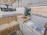 Inside a modern rv rental: bed, wood-accented kitchen with sink, and large open fridge for compact living.