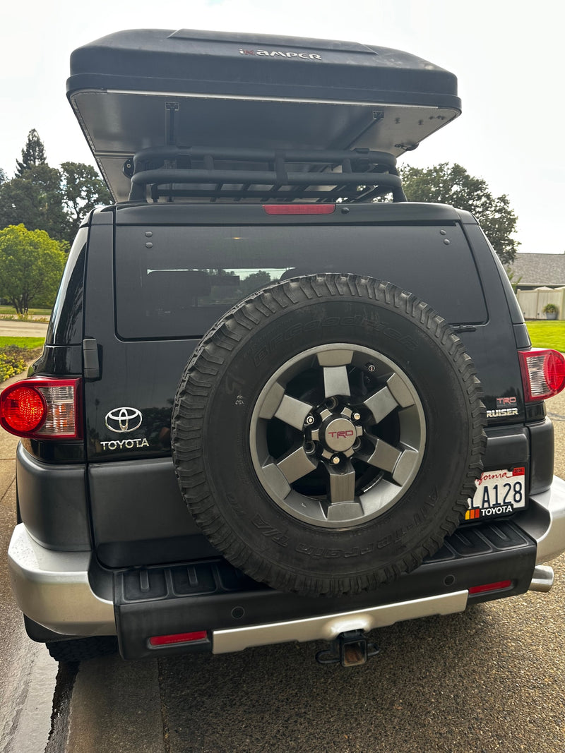 Rear view of a black Toyota FJ Cruiser SUV with an iKamper rooftop tent, perfect for an rv rental outdoor adventure. Features a spare tire and hitch. — photo 19