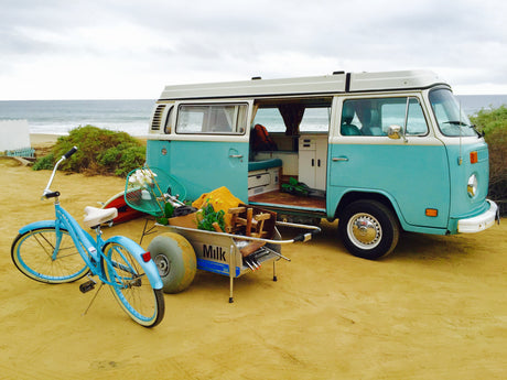 Vintage blue VW RV rental at the beach, equipped for adventure. Includes a bike & cart. Ideal for coastal escapes.