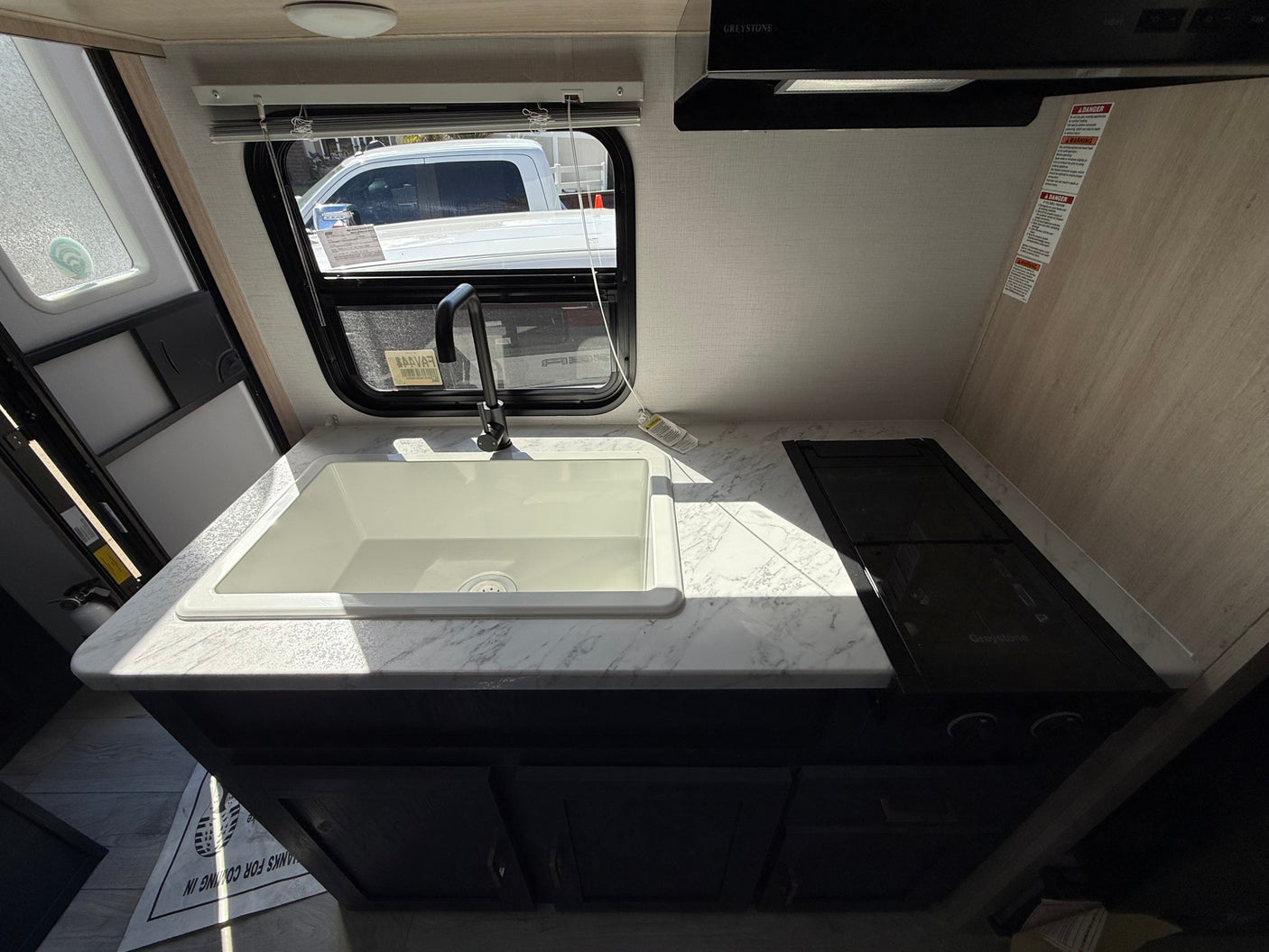 RV rental kitchen: white sink, black stovetop, Greystone range hood, and marble-style countertop, lit by a window.