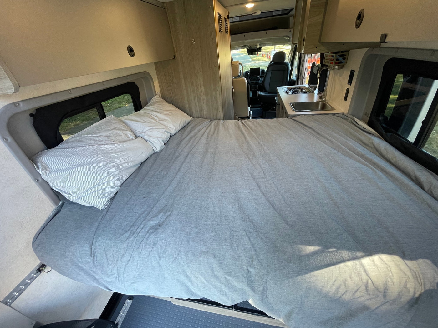 Interior of an **rv rental** showing a large bed with grey bedding, a small kitchen, and the driver's seat. — photo 11