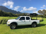 White pickup truck with a rooftop tent for rv rental, parked in a lush field with mountains in the background.