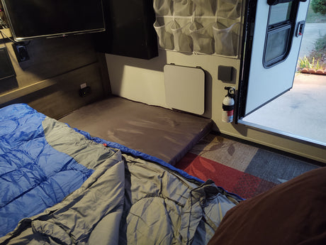 RV rental interior: cozy sleeping area with bedding, mounted TV, wall table, and fire extinguisher, ready for adventure.