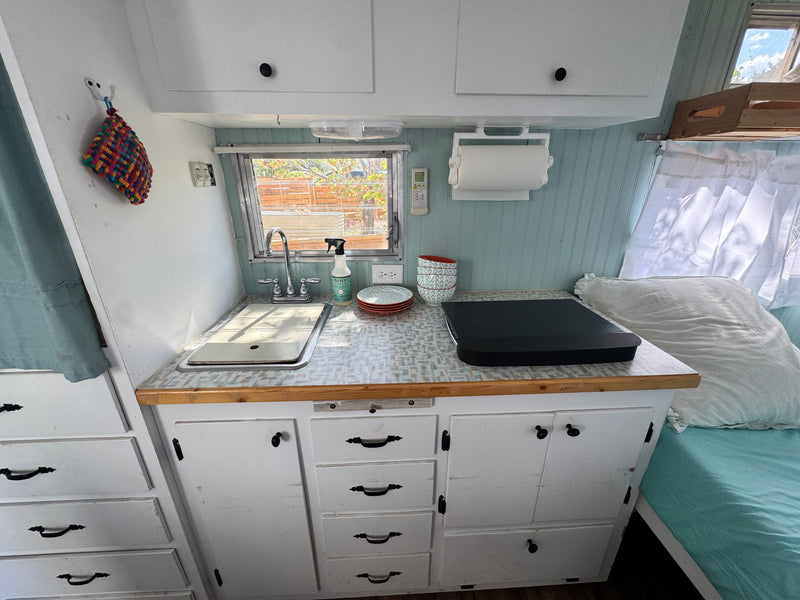 Kitchen and sleeping area inside an RV rental, showing a compact sink, counter, cabinets, and a cozy bed. — photo 4