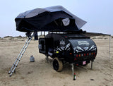 This Beyond Outdoors RV rental teardrop trailer, featuring a rooftop tent and awning, is set up for camping on sandy dunes.