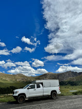 White truck with overland camper in scenic mountains under blue sky. A great RV rental alternative for outdoor adventures.