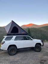 Perfect for your next RV rental adventure! A white 4Runner with a Roofnest rooftop tent overlooks vibrant mountains and forests.