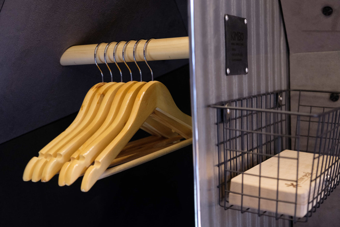 RV rental storage: Wooden hangers hang on a closet rod. A metal wire basket holds a 'Snow Peak' block, next to a 'Kimbo' plaque.