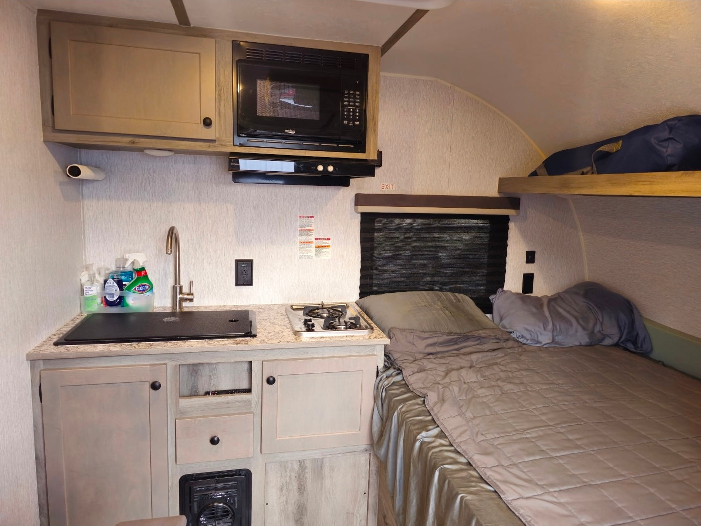 RV rental interior with compact kitchen, sink, stove, microwave, bed, and an overhead bunk.