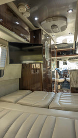 View of a modern rv rental interior with plush cream seating, a mounted TV, and sleek wood cabinetry.
