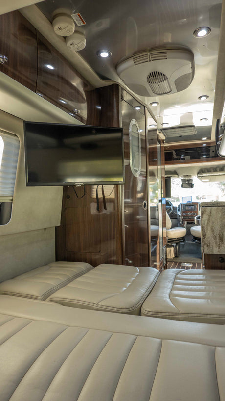 View of a modern rv rental interior with plush cream seating, a mounted TV, and sleek wood cabinetry.