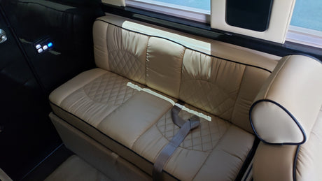 This rv rental interior features comfortable light beige quilted bench seating, a control panel with illuminated blue buttons, and a window providing natural light.