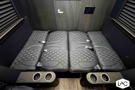 Luxury RV rental interior: plush, diamond-quilted seats laid flat as a bed, with cup holders and a sleek wooden door.