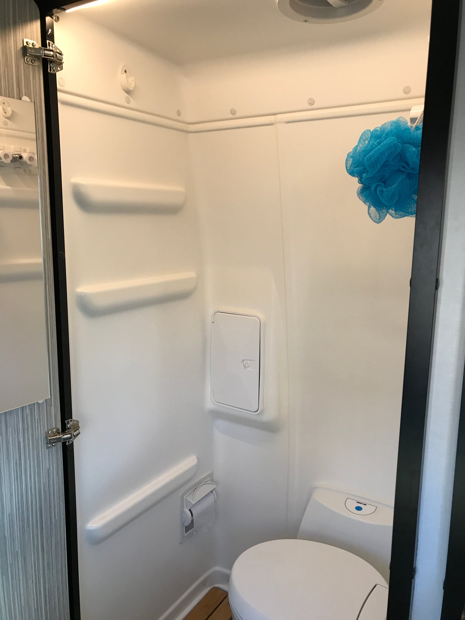Compact white RV wet bath interior with toilet, blue loofah, and built-in features, ideal for rv rental trips.