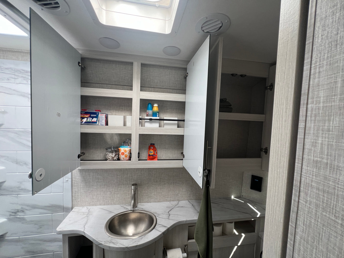 RV rental bathroom's open medicine cabinet, revealing organized first aid, cleaning supplies, and toiletries above a modern sink.