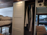 RV rental interior showing a bunk bed, open closet with clothes, and control panel on white shiplap walls.