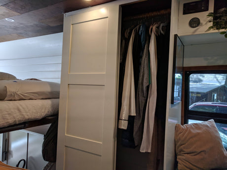 RV rental interior showing a bunk bed, open closet with clothes, and control panel on white shiplap walls.
