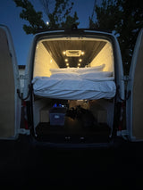 Illuminated camper van interior: a comfy raised bed above storage, ready for your next rv rental adventure.
