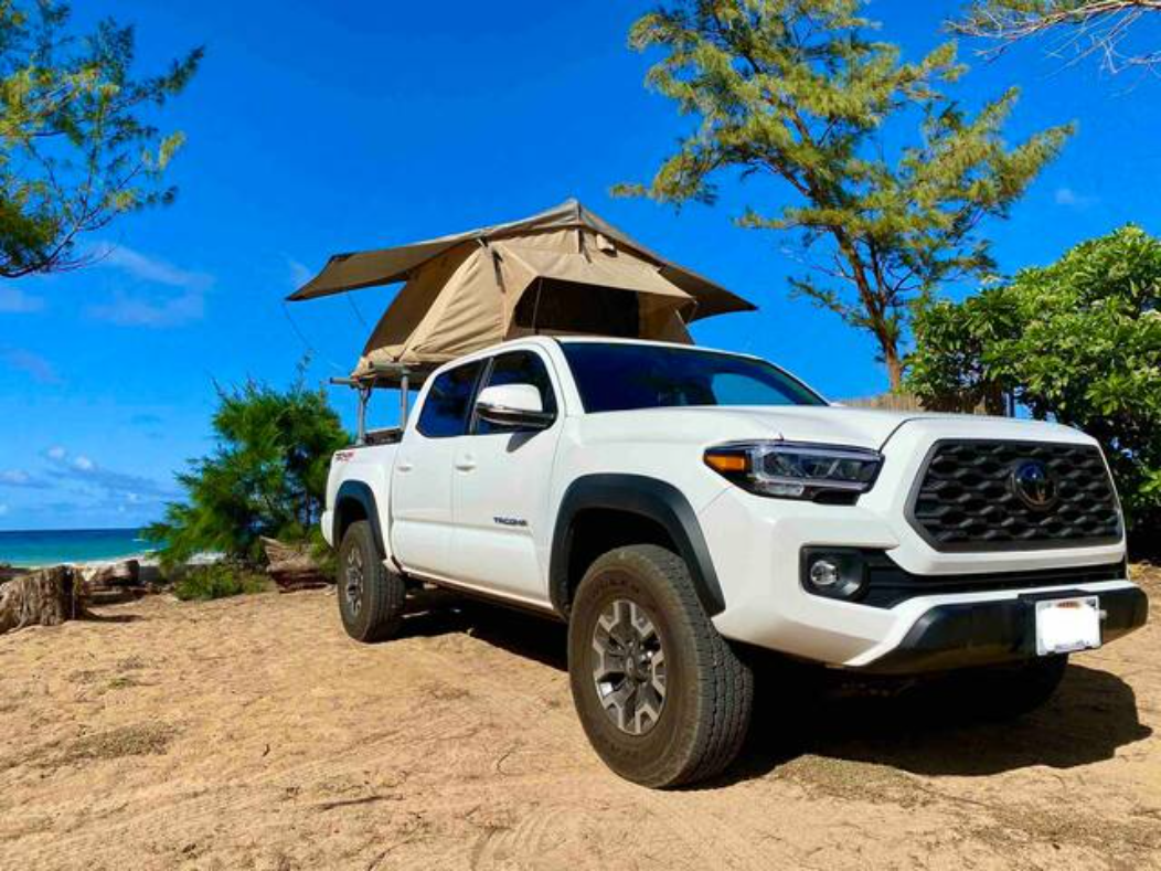 Coastal road trip ready! This white Toyota Tacoma with a rooftop tent makes an excellent RV rental for beach camping.