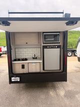This compact RV rental features a well-equipped outdoor kitchen with a microwave, fridge, sink, and stove for camping.