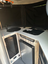 RV rental kitchen: compact design with sink, cooktop, and refrigerator. Black window shades provide privacy.