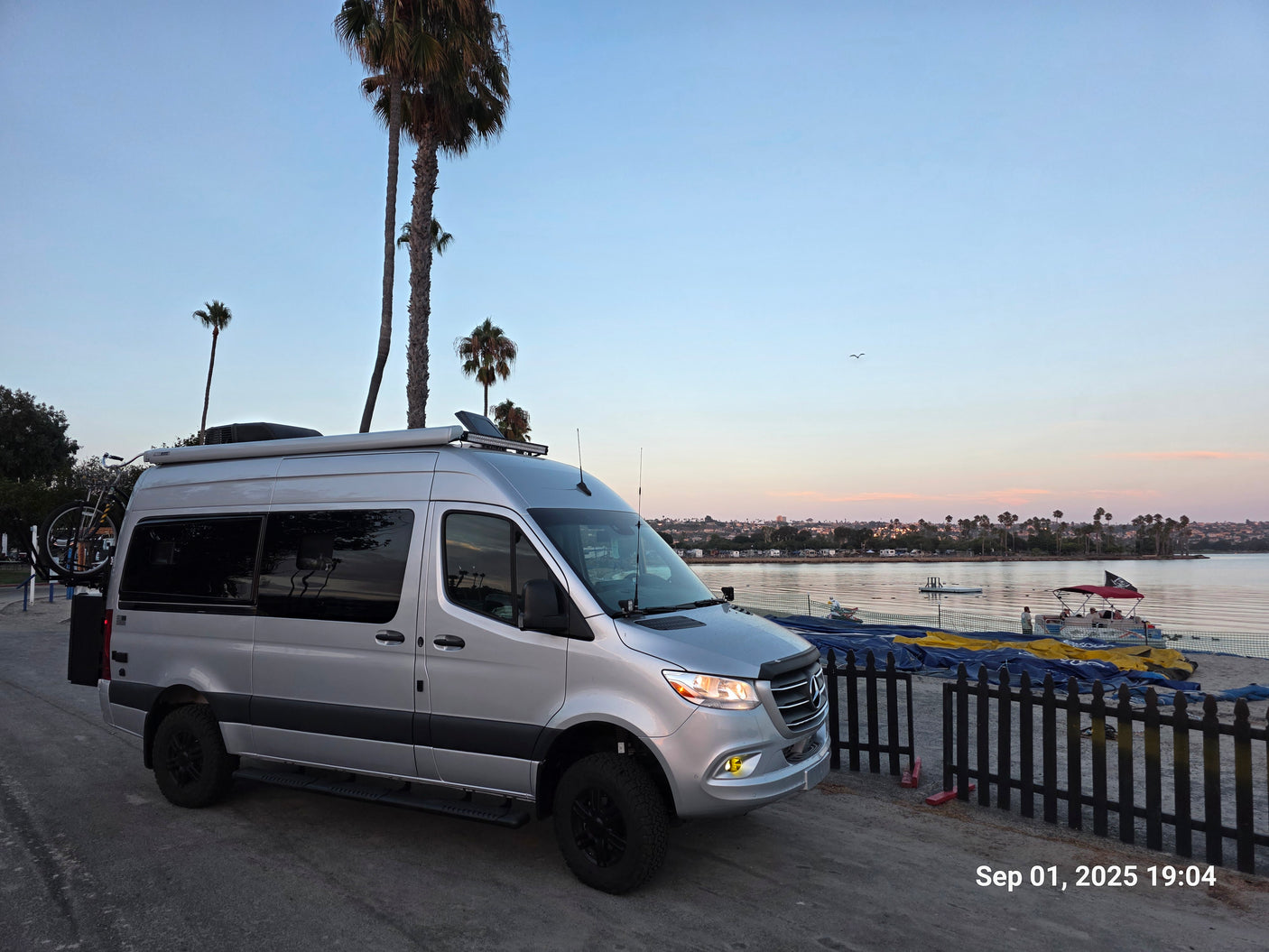 Silver Sprinter RV rental by waterfront at sunset. Palm trees frame this adventure-ready camper van.