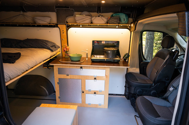 Spacious RV rental camper van interior with cozy bed, compact kitchen (stove, sink), smart storage, and front seats. — photo 15