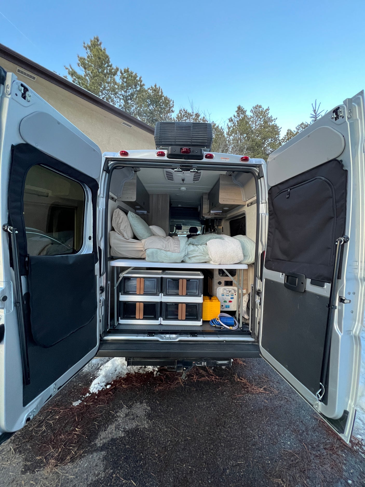 Open rear of an RV rental showing a cozy bed, organized storage, and utility panel for comfortable adventures.