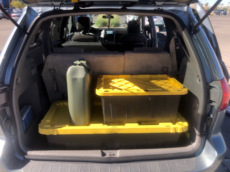 Minivan's cargo area, with folded seats, storage bins, and water jug, ready for an RV rental trip.