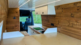 Spacious rv rental camper van interior: warm wood paneling, sleek kitchen with hob, overhead storage, and comfy bed area.