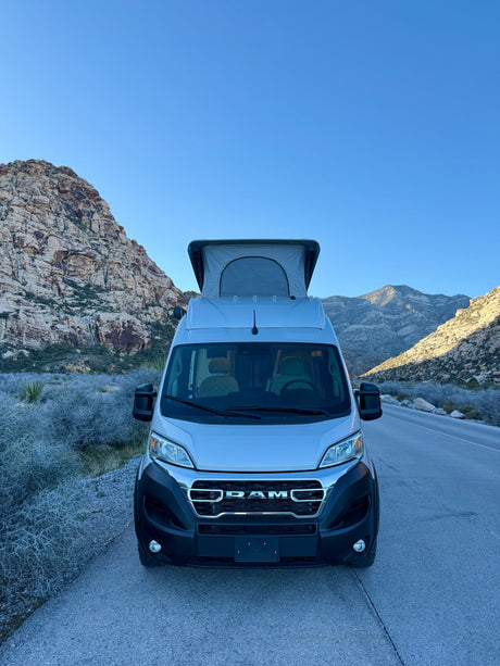 **RV rental** camper van parked by rugged mountains under a clear sky, ready for a nature road trip adventure.