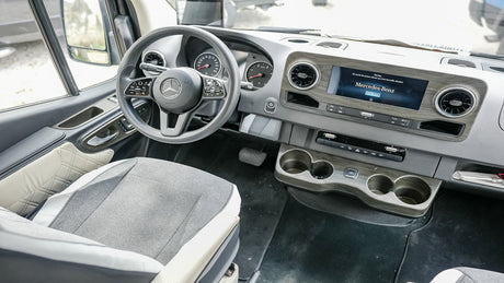 Spacious Mercedes-Benz RV rental interior with a modern dashboard, large screen, and comfortable driver's seat.