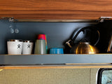 Inside an RV rental cabinet: Hydro Flasks, colorful cups, and a kettle neatly stored, ready for travel.