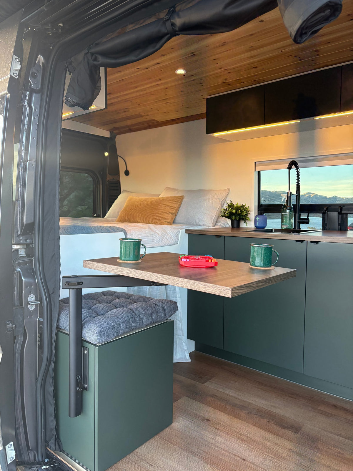 Inside a modern RV rental: cozy bed, compact kitchen, and clever table setup with a beautiful window view. — photo 11