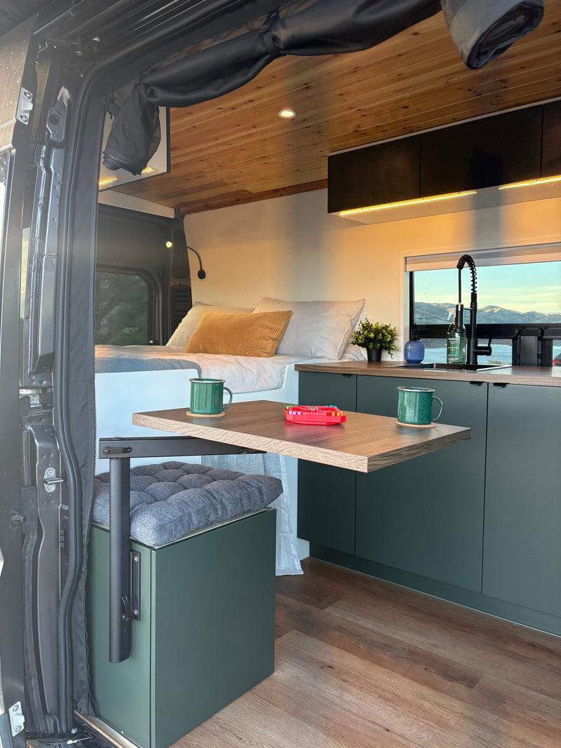 Inside a modern RV rental: cozy bed, compact kitchen, and clever table setup with a beautiful window view. — photo 11