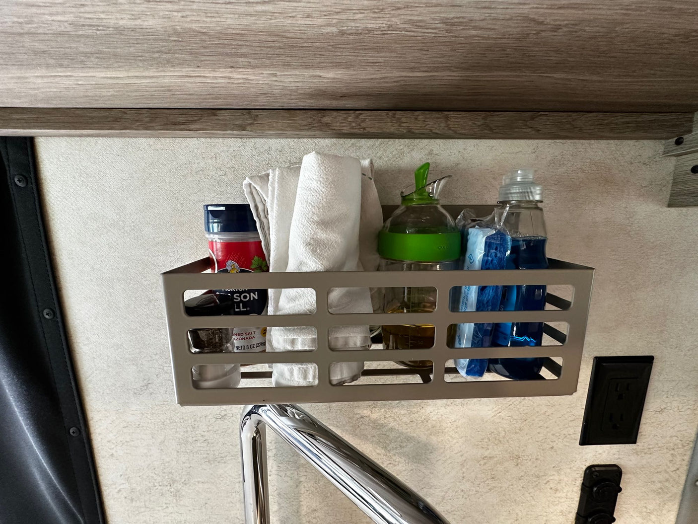 In an RV rental, a wall-mounted basket neatly organizes kitchen essentials: salt, oil, dish soap, and towels for compact storage.