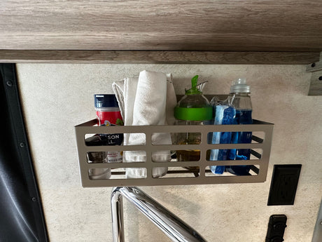 In an RV rental, a wall-mounted basket neatly organizes kitchen essentials: salt, oil, dish soap, and towels for compact storage.