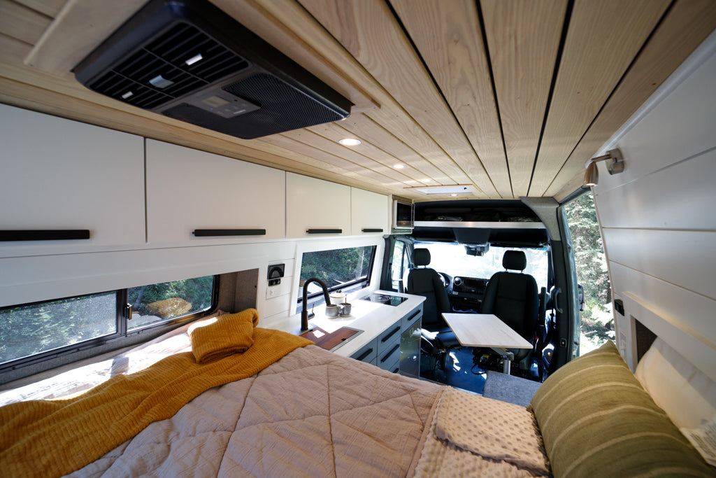 Interior of a stylish modern RV rental van with a comfortable bed, full kitchen, and dining area, ready for adventure.