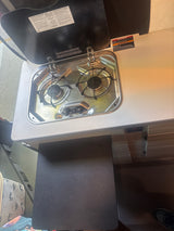 This RV rental features a 2-burner Suburban gas stove with safety warnings and lighting instructions visible on its open lid, ideal for a travel trailer kitchenette.