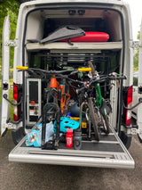 Inside an RV rental: multiple mountain bikes securely stored on an extended tray, with adventure gear and bedding visible.