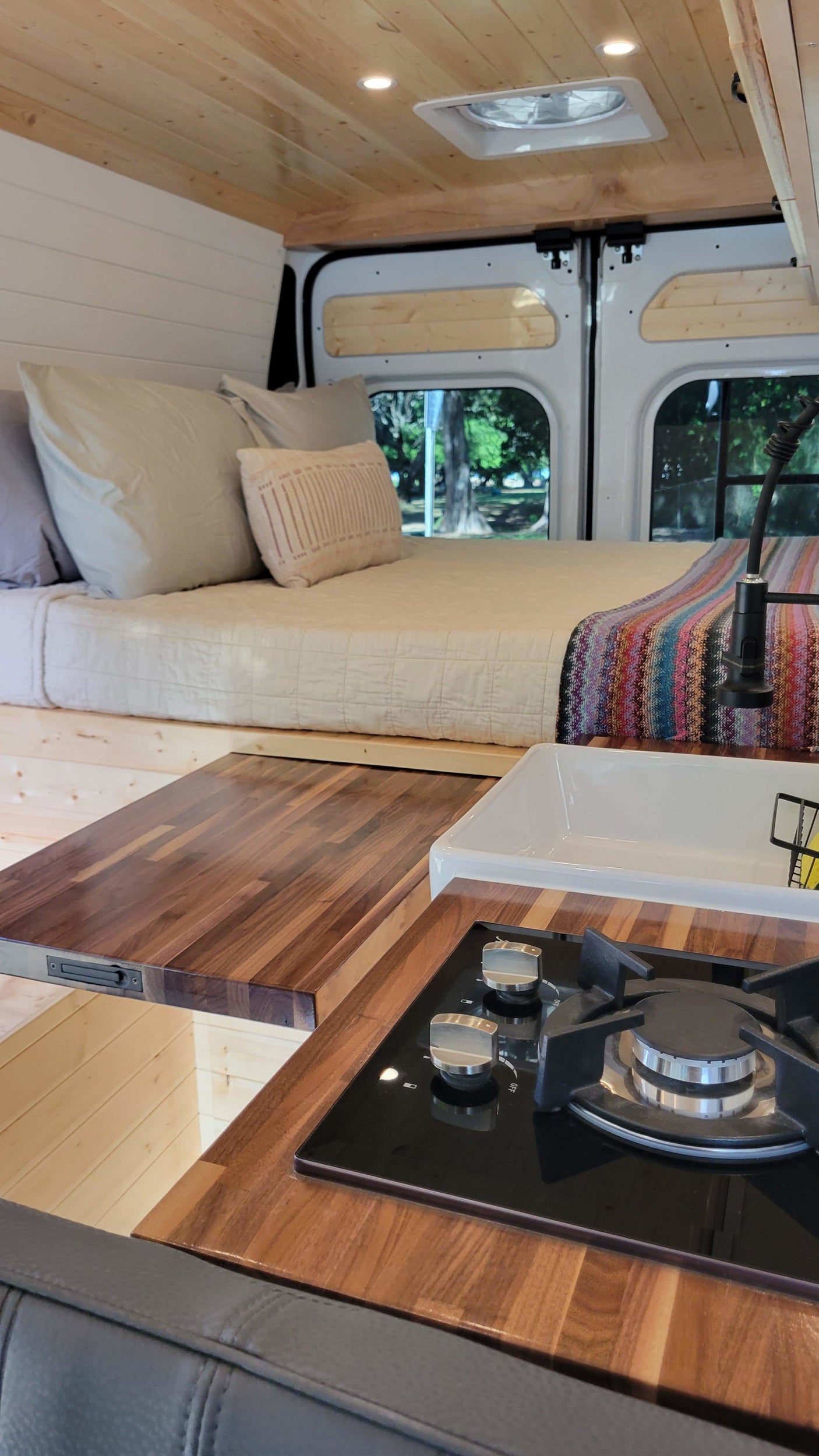 Explore in comfort! This RV rental features a cozy bed, sleek kitchen with stove & sink, and warm wood accents.