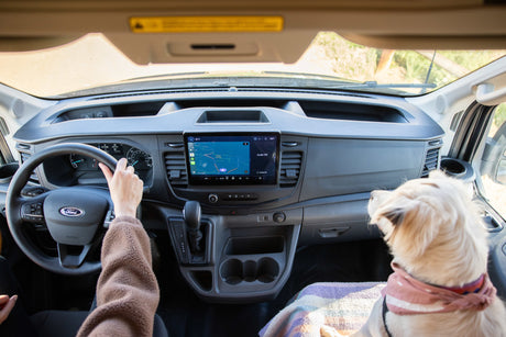 RV rental interior: A person drives a Ford van with a dog co-pilot, viewing navigation on the infotainment screen.