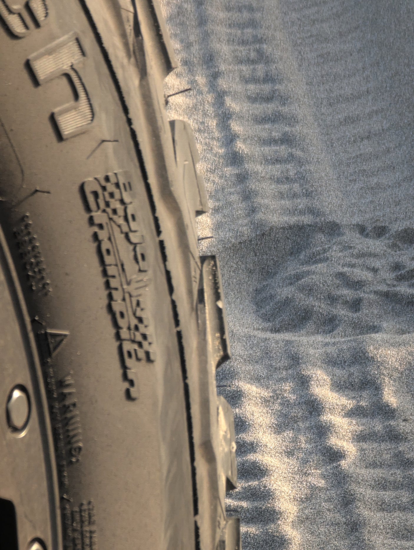 Close-up of an RV rental tire (Gravel Commander) on rippled sand, ready for your next adventure.