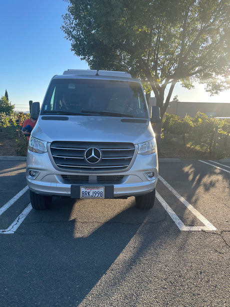 Head-on view of a silver Mercedes-Benz Sprinter van, an RV rental, parked in a sunny lot.