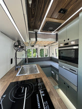 Inside this modern RV rental: a compact kitchen with induction cooktop, sink & appliances. Versatile interior with bed and seating.