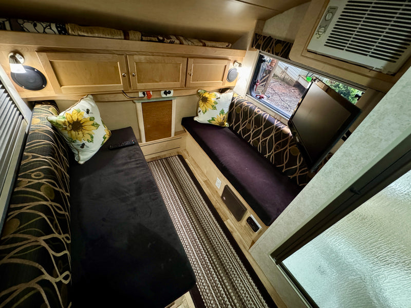 Inviting RV rental interior showcasing comfortable benches, sunflower pillows, overhead storage, AC, and a window. — photo 12