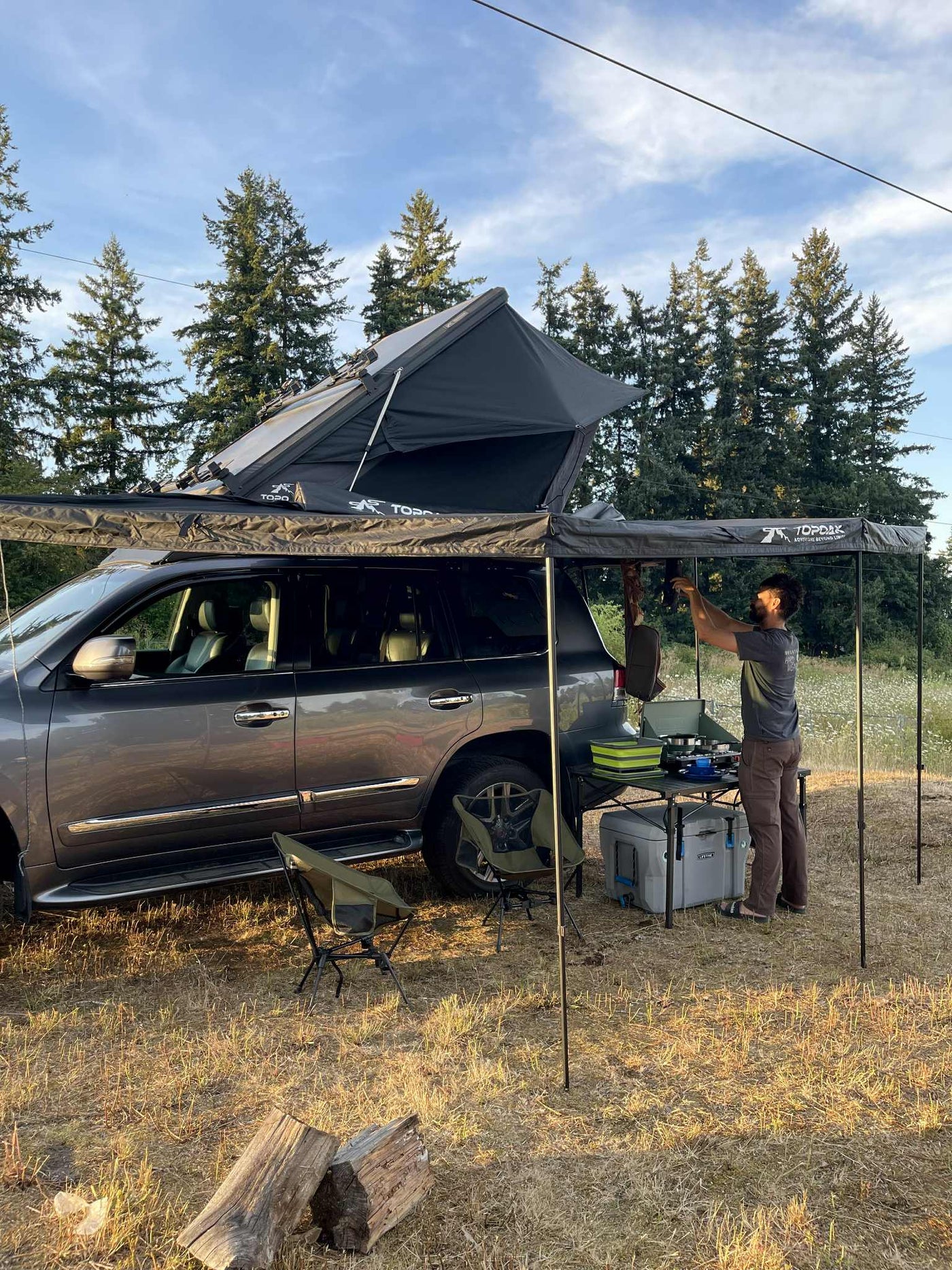 Man sets up an outdoor kitchen from an SUV with a rooftop tent & awning – a compact RV rental-style camp. — photo 7