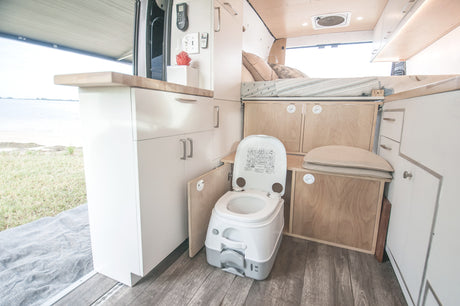 Inside an rv rental: functional interior with a portable toilet, cozy bed, and kitchenette, offering scenic views outdoors.